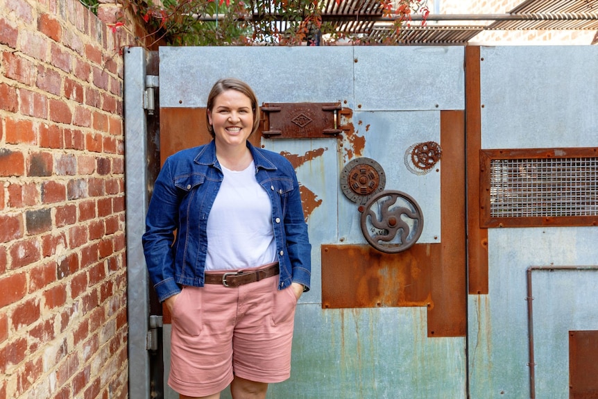 L'éducatrice financière et auteure Lacey Filipich sourit debout à côté d'un mur de briques.